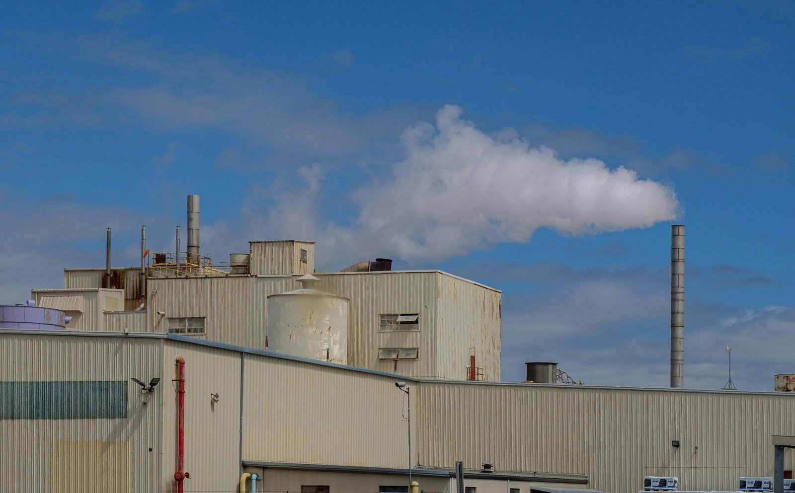 A large industrial factory emitting smoke from chimneys under a clear blue sky.